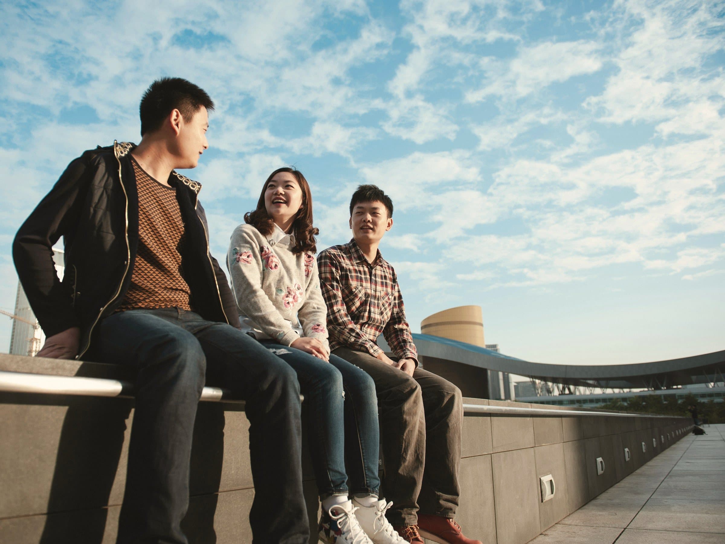 Three students chatting on a sunny campus terrace.